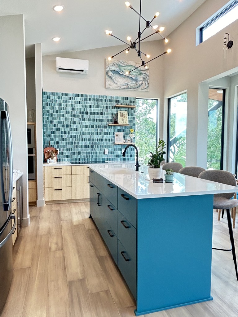 Long Beach, MS new construction with a teal island, white oak flooring, bamboo cabinets, white quartz countertops, modern light fixture, teal backsplash by Elizabeth Hall Designs